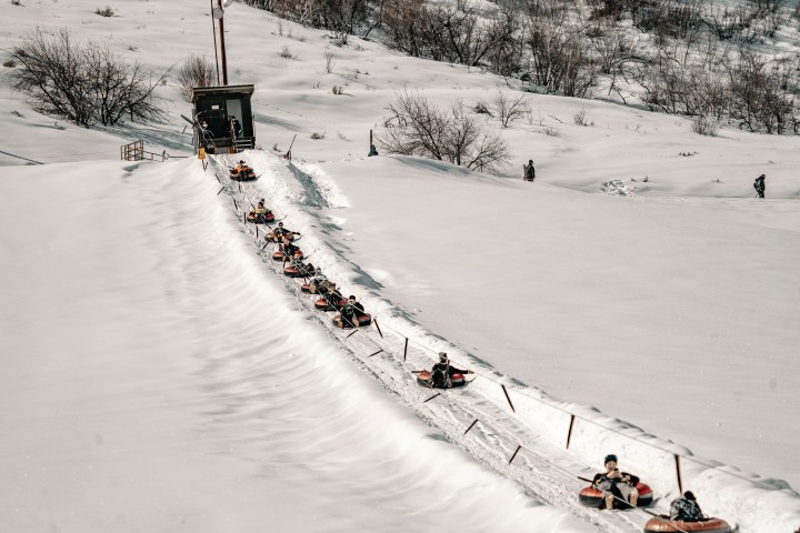 People snow tubing uphill on a conveyor belt in a snowy landscape.