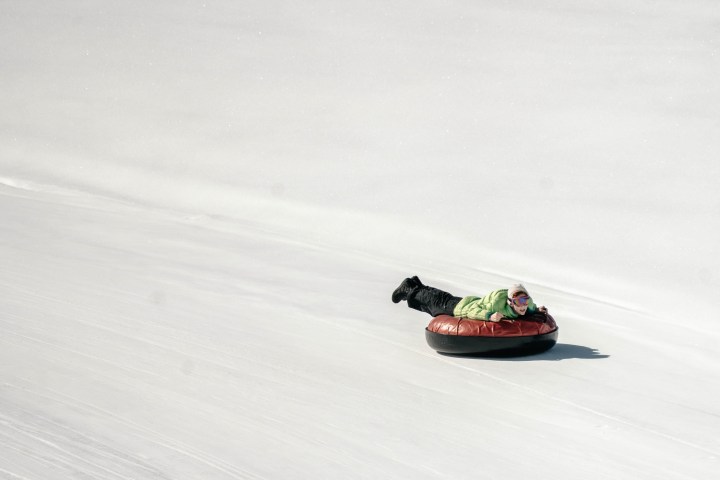 Person sledding on a snow tube downhill in a snowy landscape.