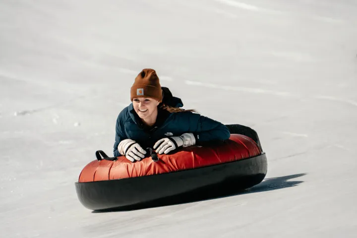 Person in winter clothes sliding downhill on a red snow tube.