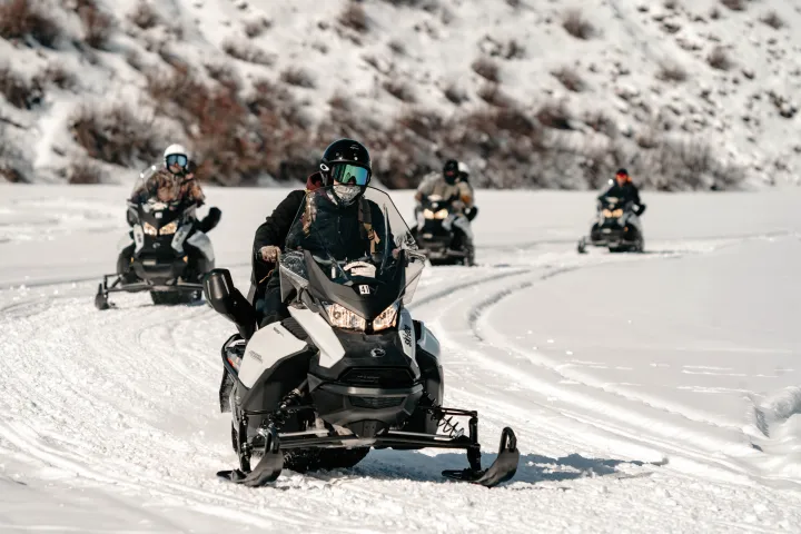 Group of people riding snowmobiles on a snowy terrain.