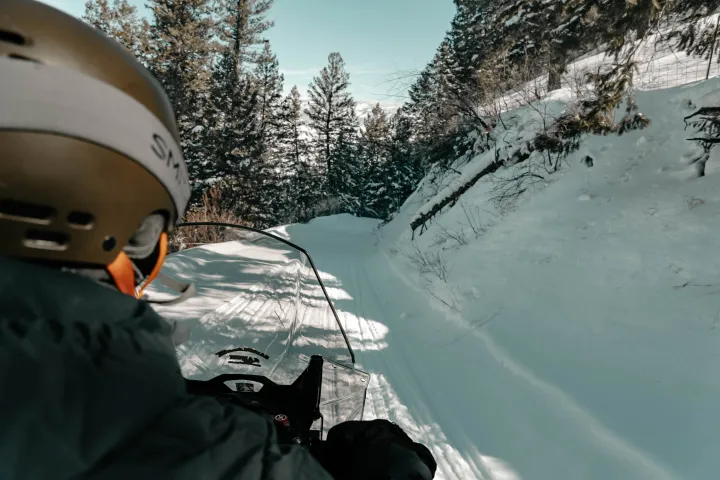 Person on a snowmobile riding through a snowy forest trail.