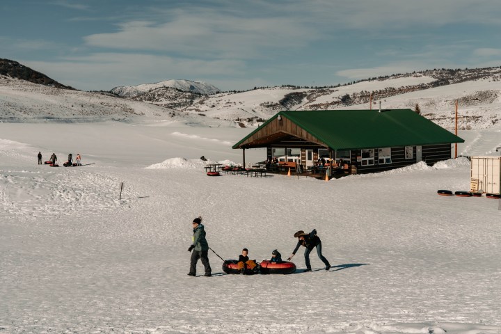 Snowy landscape with people tubing near a cabin with a green roof.