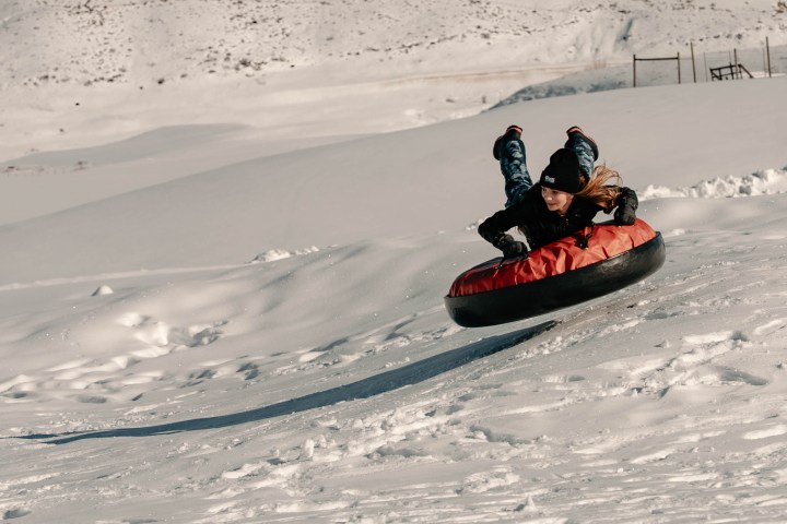 Person in winter gear tubing down snowy slope on a red inflatable tube.