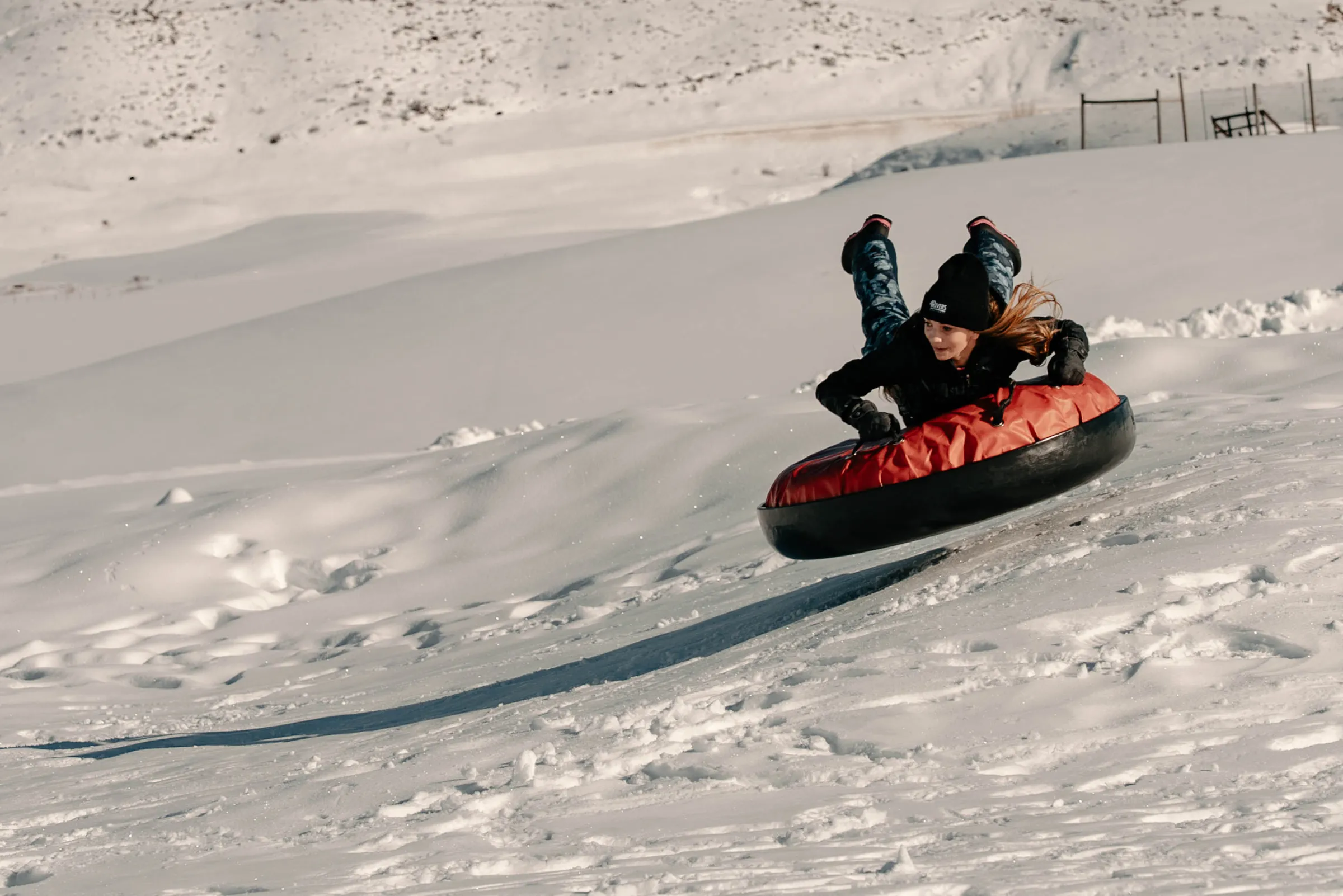 Person in winter gear tubing down snowy slope on a red inflatable tube.