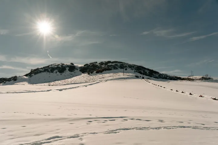 Sunny winter landscape with a snow-covered hill and clear blue sky.