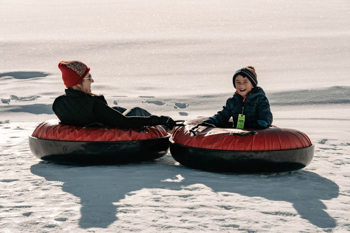 Two people tubing on snow, one adult and one child, wearing winter clothes and smiling.