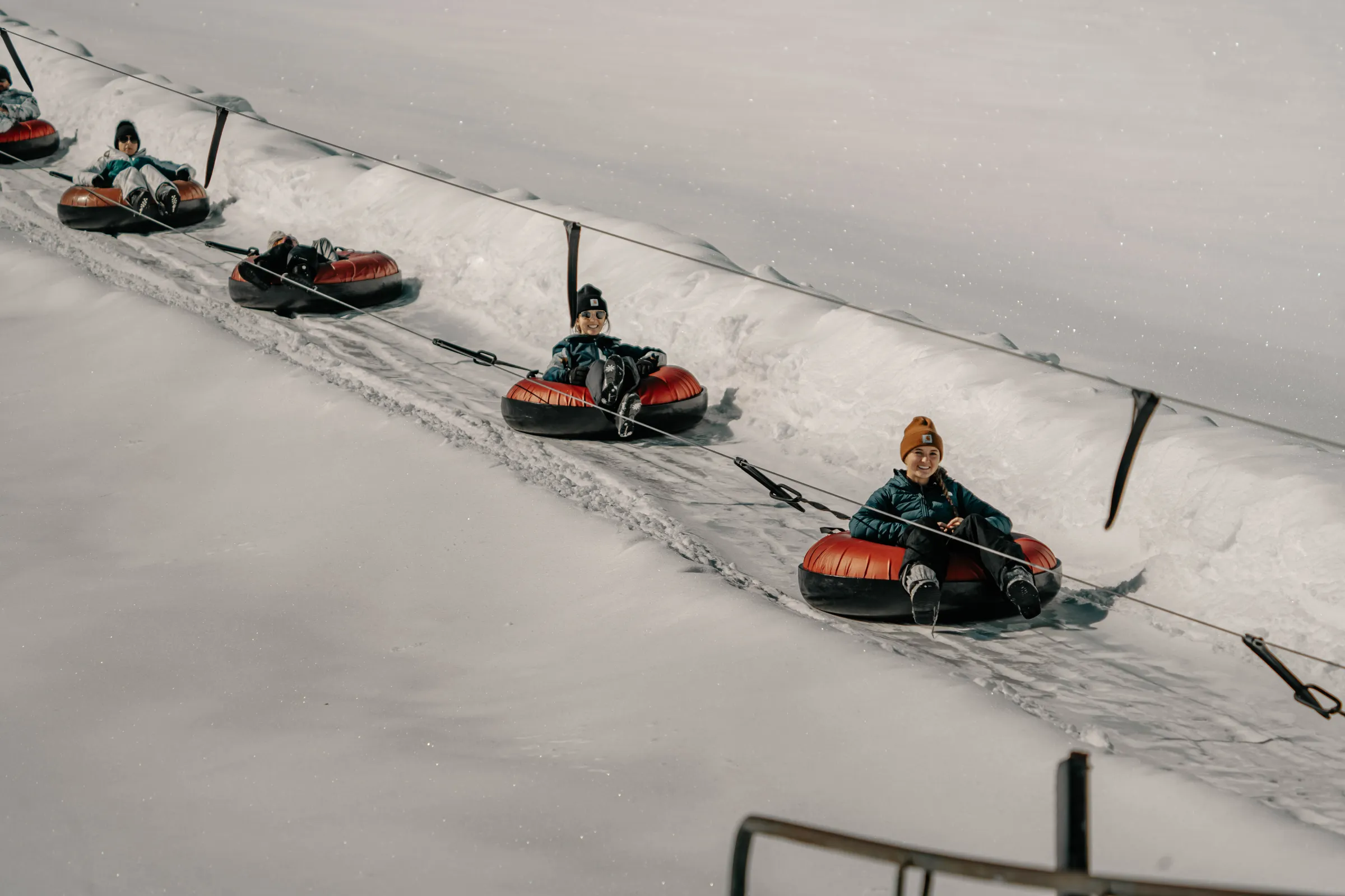 People riding snow tubes on a conveyor belt in a snowy landscape.