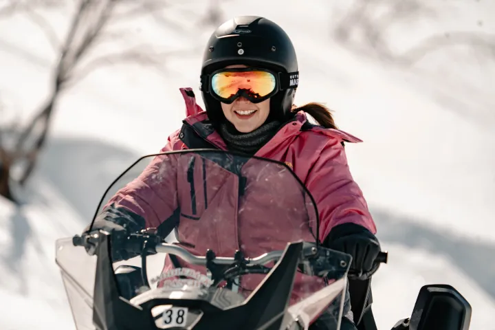 Person in a pink coat riding a snowmobile on a snowy landscape.