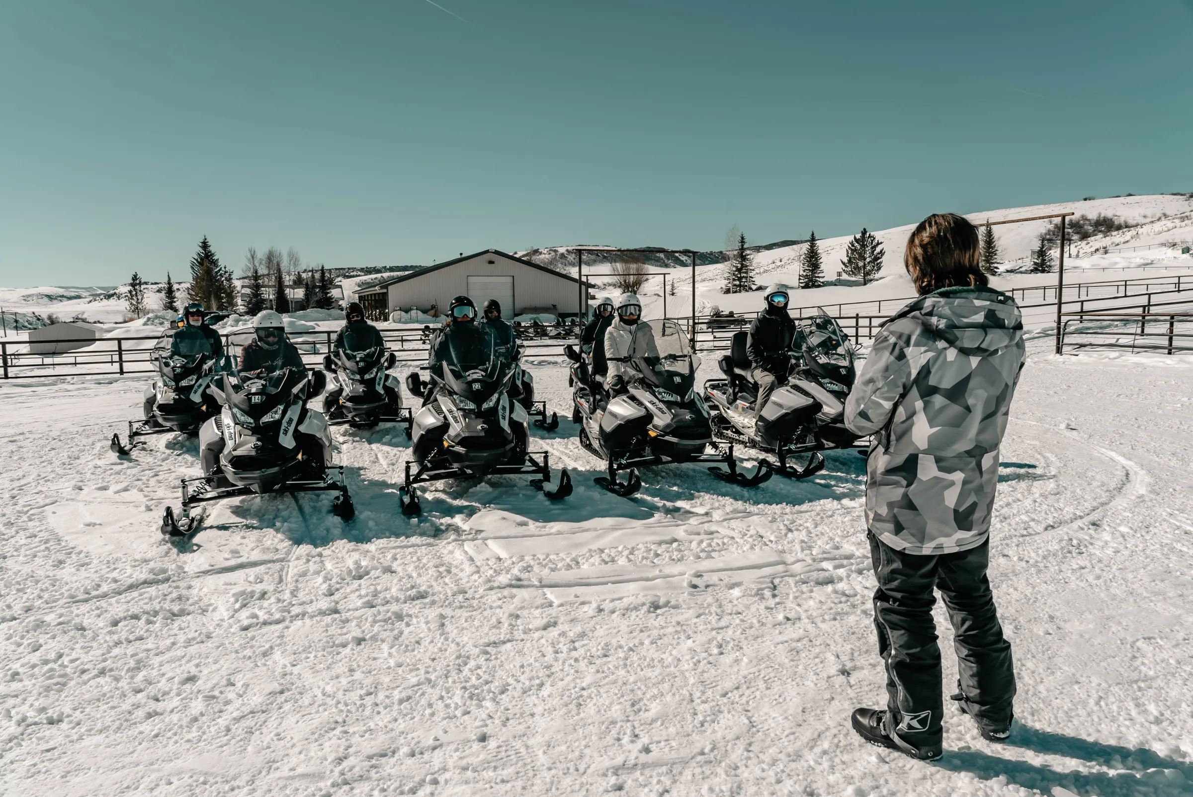 Group of people on snowmobiles in snowy landscape with clear sky.