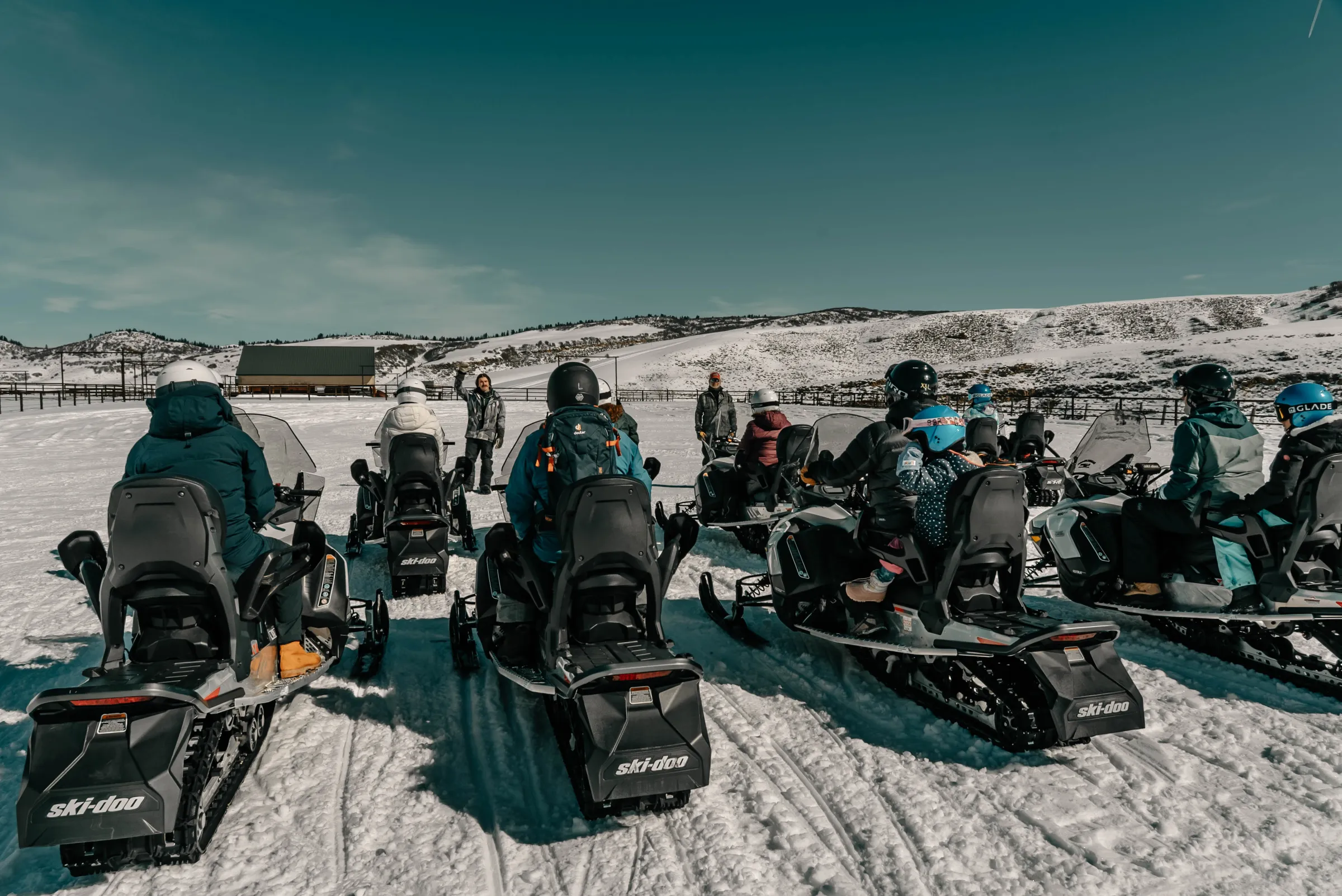 Group of people on snowmobiles in a snowy landscape under a clear sky.